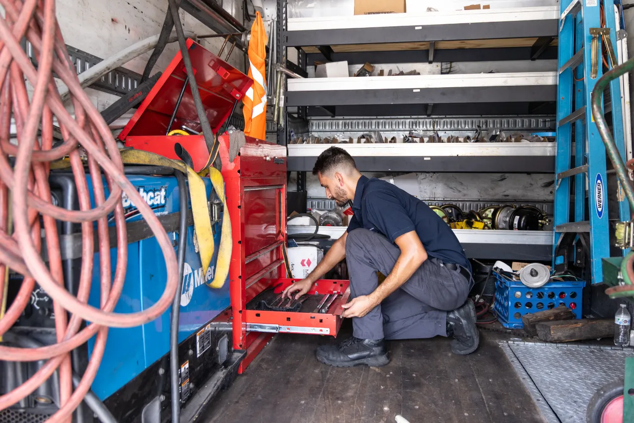 Mobile truck repairs in Broward County, FL: technician kneels in service truck pulling tools from red toolbox beside Bobcat welder.