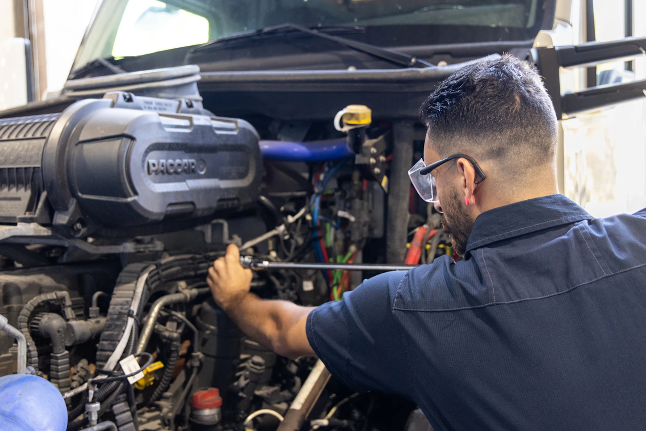 Diesel engine repair with technician working on PACCAR engine components inside semi truck engine bay during service.